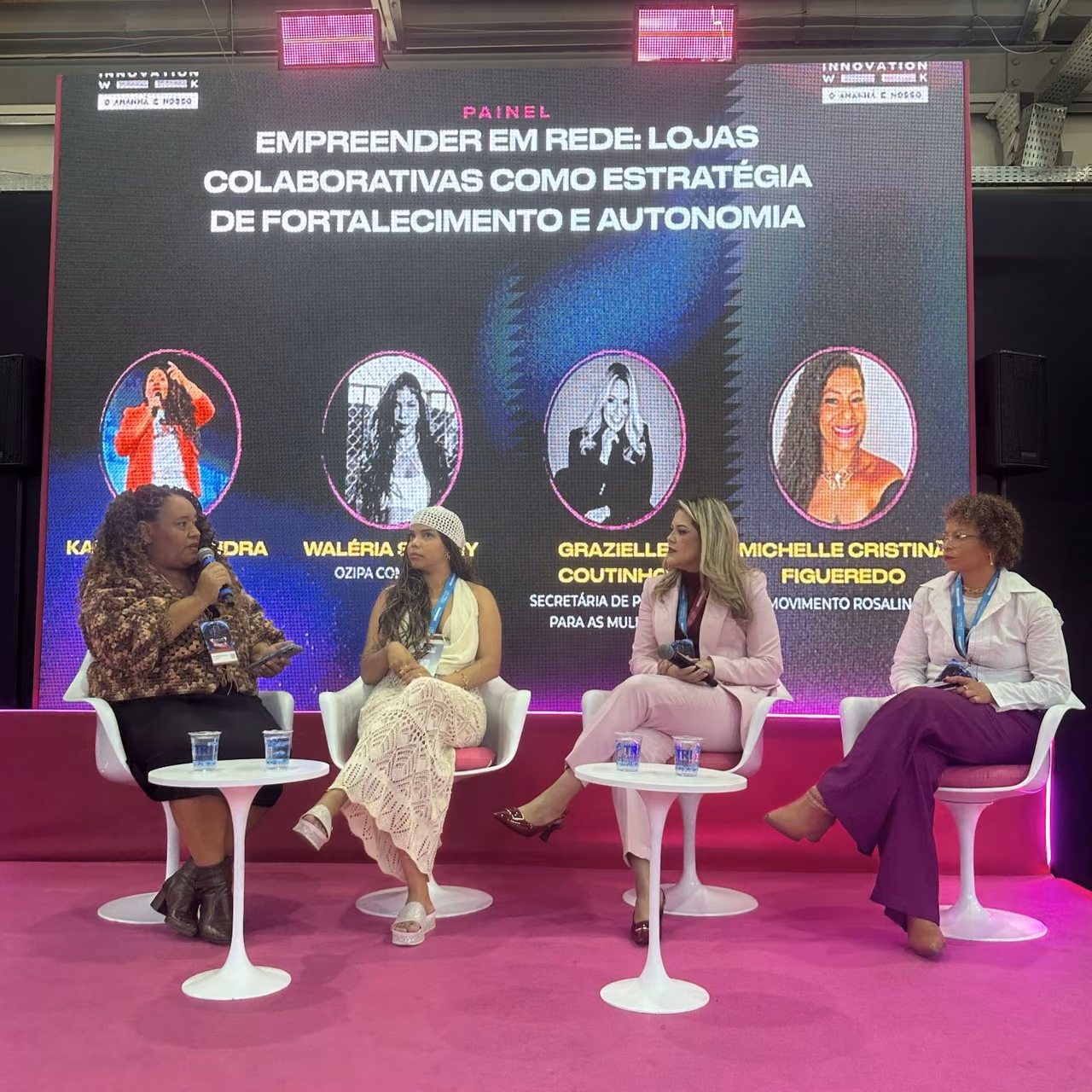 Quatro mulheres participam de uma roda de conversa no palco do Campinas Innovation Week 2026. Karla Marques está à esquerda, segurando um microfone, ao lado de três participantes. Ao fundo, um painel apresenta o tema “Empreender em rede: lojas colaborativas como estratégia de fortalecimento e autonomia”.